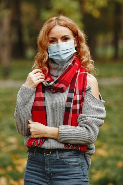 Mujer en bosque otoñal. Persona con máscara. Tema de coronavirus. Dama con un pañuelo rojo.