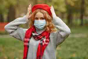 Foto gratuita mujer en bosque otoñal. persona con máscara. tema de coronavirus. dama con un pañuelo rojo.