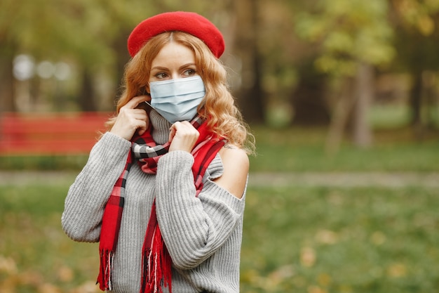 Mujer en bosque otoñal. Persona con máscara. Tema de coronavirus. Dama con un pañuelo rojo.