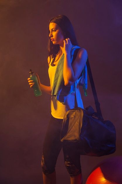 Foto gratuita mujer con botella y bolsa en cuarto oscuro