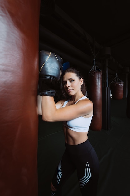 Mujer de boxeo posando con saco de boxeo, en cuarto oscuro. Concepto de mujer fuerte e independiente