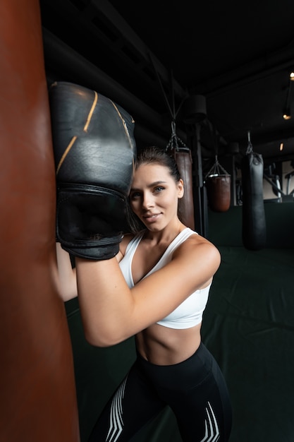 Mujer de boxeo posando con saco de boxeo, en la oscuridad. Concepto de mujer fuerte e independiente