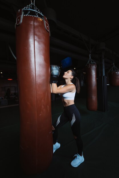 Mujer de boxeo posando con saco de boxeo, en la oscuridad. Concepto de mujer fuerte e independiente