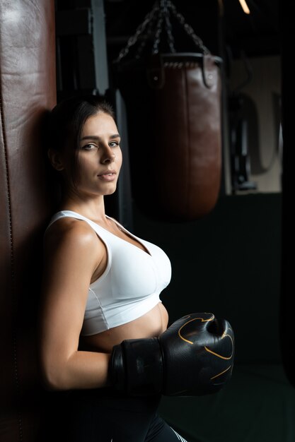 Mujer de boxeo posando con saco de boxeo, en la oscuridad. Concepto de mujer fuerte e independiente