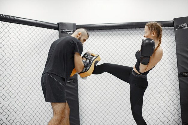 Mujer de boxeo. Principiante en un gimnasio. Dama en ropa deportiva negra. Mujer con entrenador.