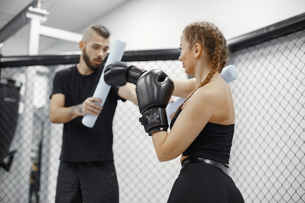 Mujer de boxeo. Principiante en un gimnasio. Dama en ropa deportiva negra. Mujer con entrenador.