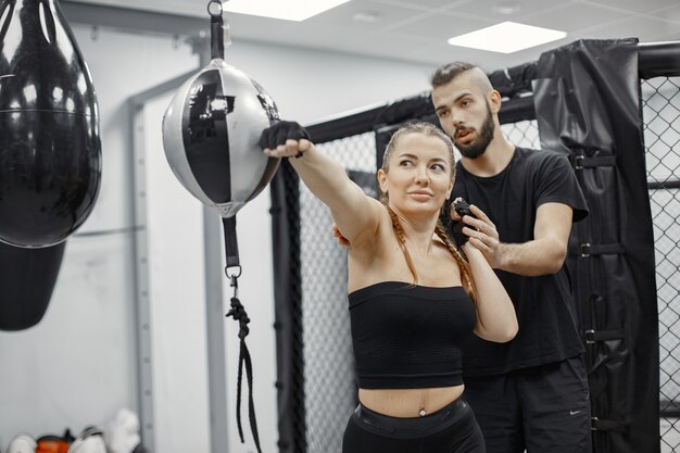 Mujer de boxeo. Principiante en un gimnasio. Dama en ropa deportiva negra. Mujer con entrenador.