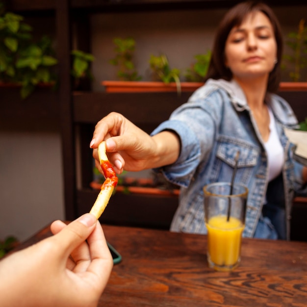 Mujer brindando con su amiga usando papas fritas con salsa de tomate