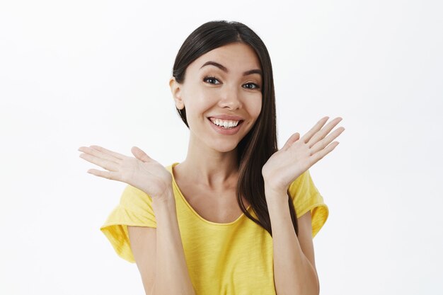 Mujer bronceada femenina atractiva hermosa y feliz con el pelo oscuro levantando las palmas a un lado y sonriendo ampliamente
