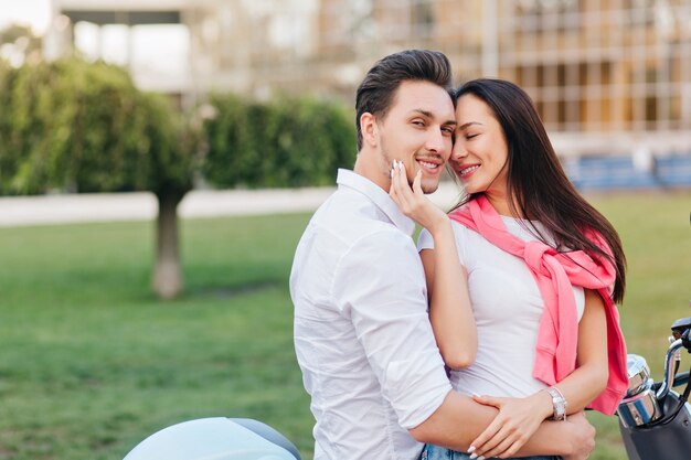 Mujer bronceada con hermosa sonrisa tocando la mejilla del novio con los ojos cerrados