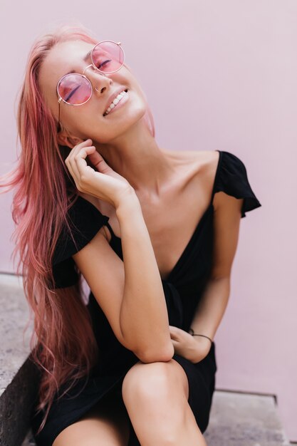 mujer bronceada sonriendo durante la sesión de fotos al aire libre en vestido negro.