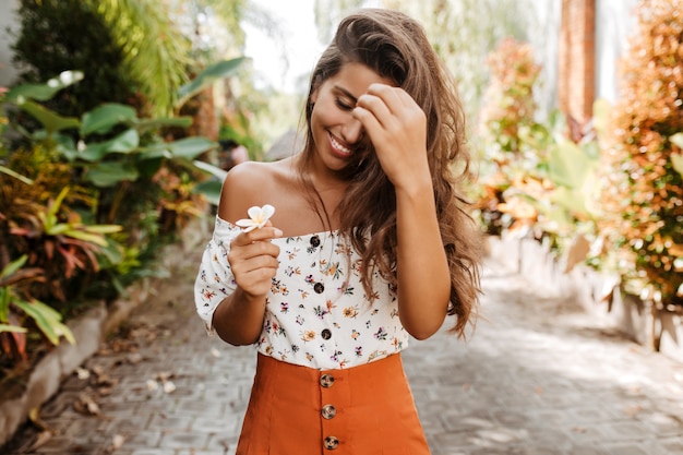 Mujer bronceada de vacaciones mira flor blanca con sonrisa