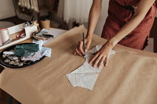 Mujer bronceada con vestido rojo de lino dibuja un patrón de tela en papel artesanal el diseñador de moda crea una muestra de ropa en la oficina