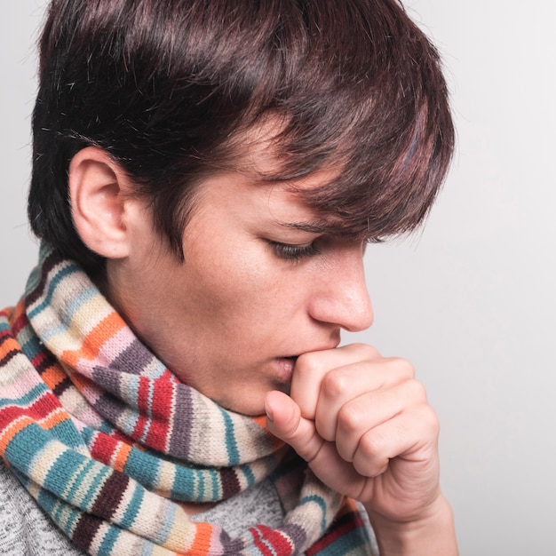 Mujer con bufanda multicolor alrededor de cuello tos sobre fondo gris