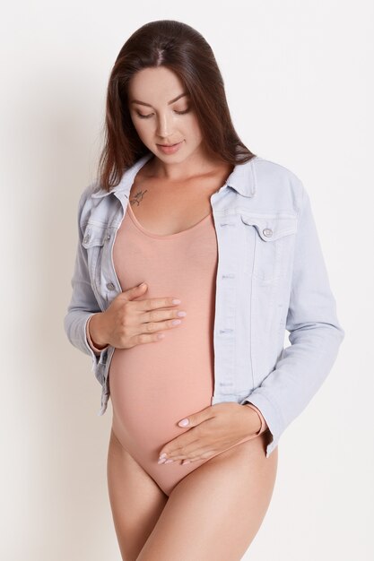 Mujer de cabello castaño suave esperando bebé, posando
