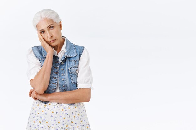 Mujer con cabello gris peinado, apoyarse en la palma de la mano, mirar a la cámara molesta con leve fatiga o irritación, estar de pie disgustada