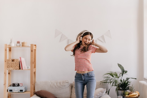 Foto gratuita mujer con un cabello hermoso y maquillaje suave baila en su habitación escuchando música