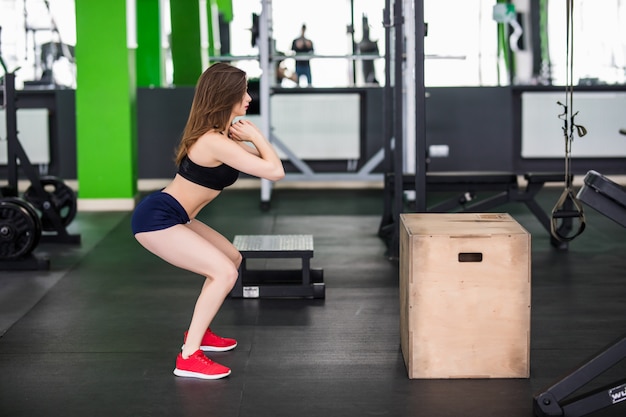 Mujer con cabello largo está trabajando con simulador de deporte paso a paso en gimnasio