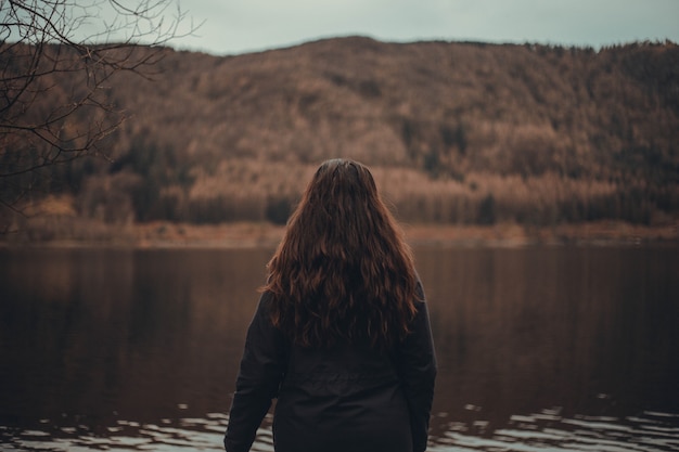 Mujer con cabello largo mirando un hermoso lago en un bosque