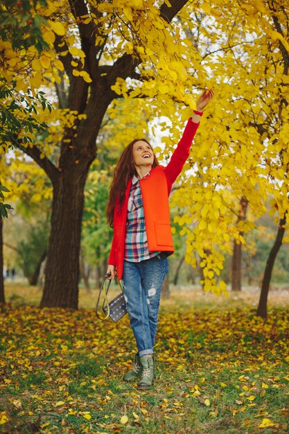 Mujer con cabello largo ondulado disfrutando de otoño en el parque.