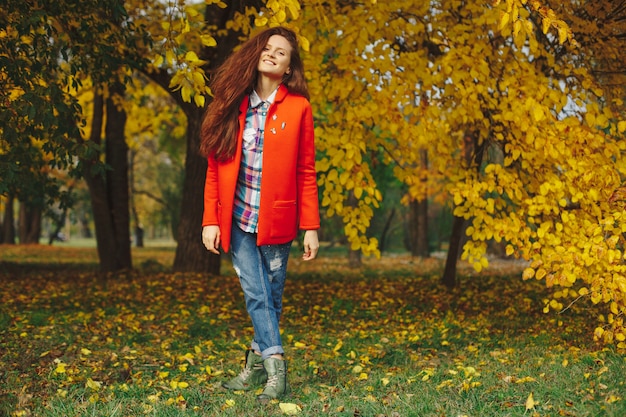 Mujer con cabello largo ondulado disfrutando de otoño en el parque.