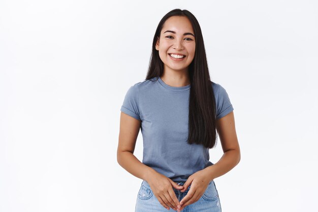 Mujer con cabello largo y oscuro y saludable, juntar las manos sobre el cuerpo y sonriendo amigable con la cámara, hablando con un amigo, teniendo una agradable conversación