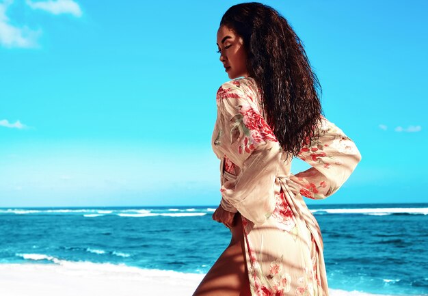 Mujer con cabello largo oscuro en vestido beige posando en la playa de verano