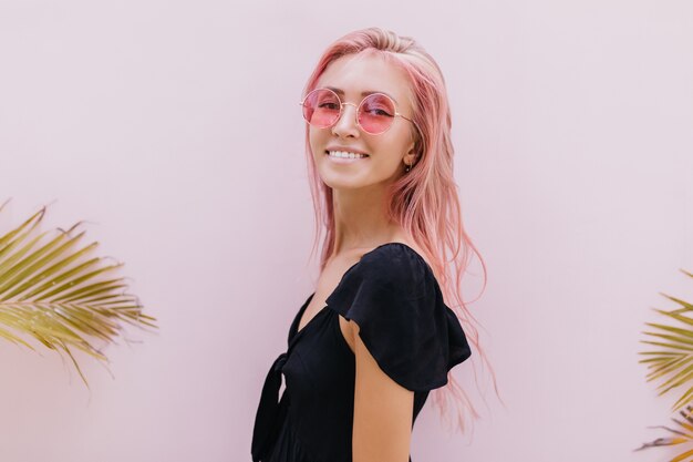 mujer con cabello largo rosa de pie junto a palmeras exóticas en estudio.