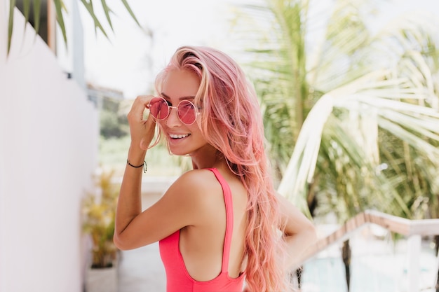 Mujer con cabello largo rosa posando con gafas de sol en la naturaleza