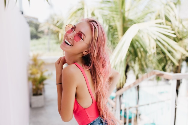 Mujer con cabello largo rosa posando con gafas de sol en la naturaleza