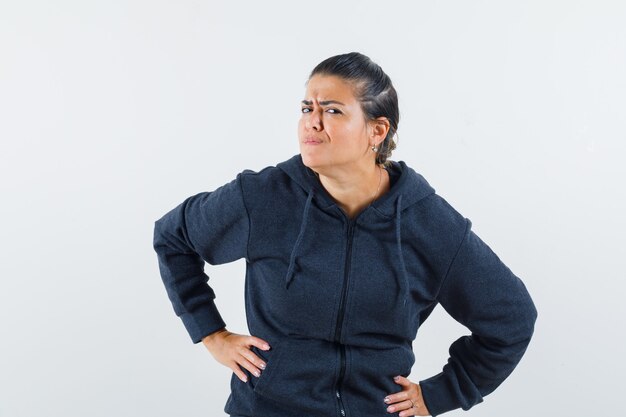 Mujer de cabello oscuro en chaqueta tomados de la mano en la cintura mientras mira cuidadosamente a la cámara y mira enfocado