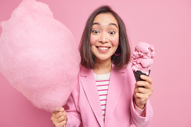 Mujer con cabello oscuro posa con sabroso postre dulce tiene algodón de azúcar y helado vestida formalmente