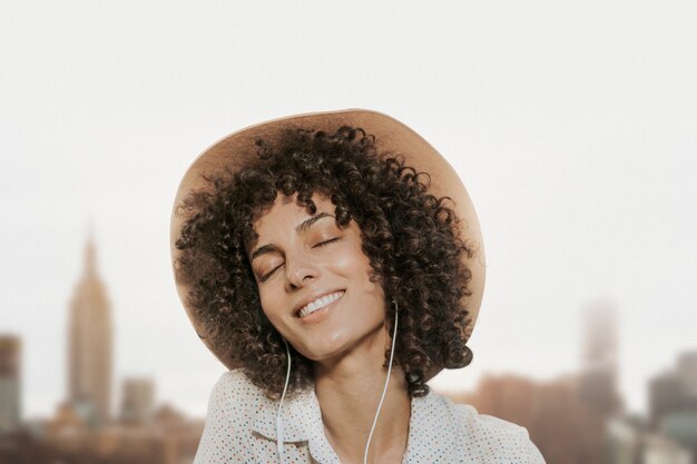 Mujer con cabello rizado con auriculares remezclados multimedia con vistas a la ciudad