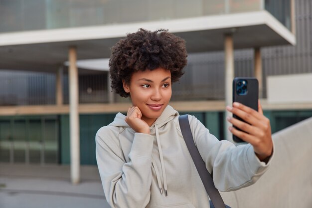 mujer con cabello rizado mira directamente a la cámara del teléfono inteligente hace videollamadas graba video blog sobre deportes charlas con seguidores da consejos sobre estilo de vida saludable