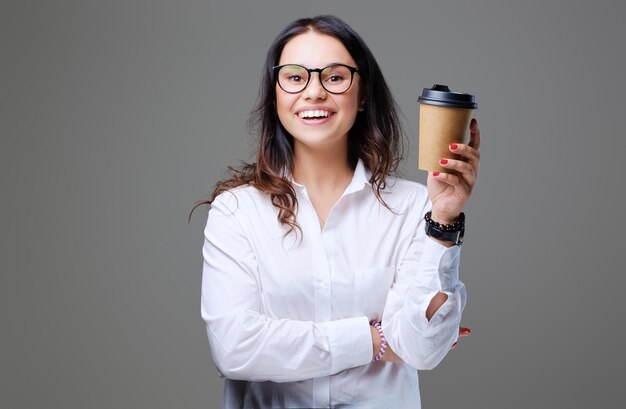 Mujer con cabello rizado oscuro y anteojos sostiene café para llevar.