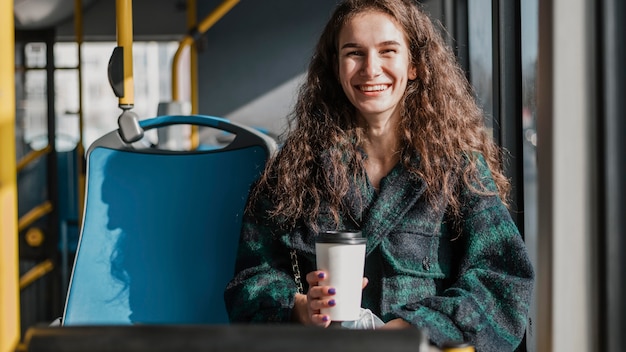 Mujer con cabello rizado sosteniendo un café en el autobús