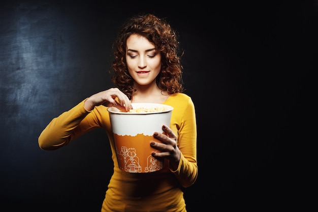 Mujer con cabello rizado toma palomitas de maíz mordiendo su parte inferior