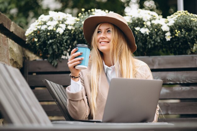 Mujer en café de consumición del sombrero y trabajando en la computadora portátil afuera