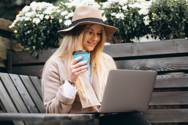 Foto gratuita mujer en café de consumición del sombrero y trabajando en la computadora portátil afuera