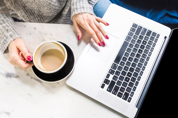 Mujer con café en la mano usando la computadora portátil