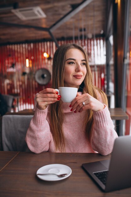 Mujer en café tomando café y trabajando en una computadora