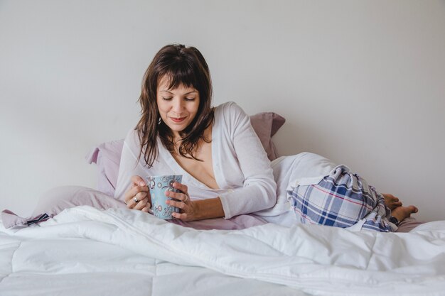 Mujer con café tumbada encima de la cama