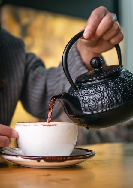 Foto gratuita mujer en un café vierte té de una tetera de hierro fundido negro