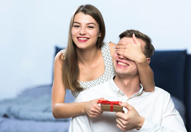 Mujer con caja de regalo que cubre los ojos del hombre.