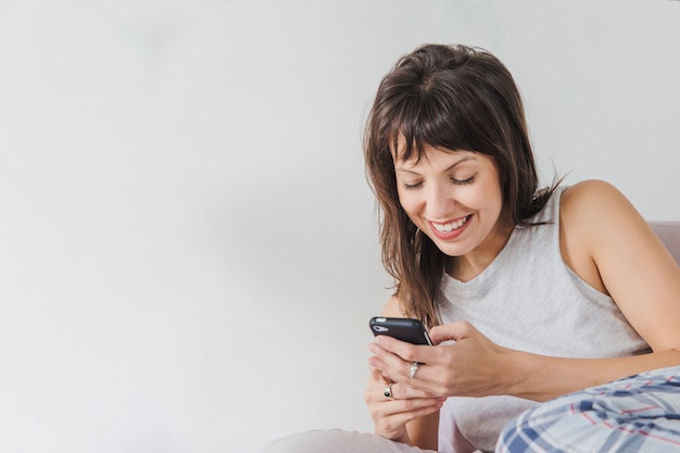 Mujer en la cama escibiendo en smartphone