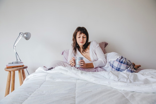 Mujer en cama mirando a su café