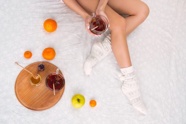 mujer en la cama con una taza de té y frutas, vista superior. Piernas femeninas en cálidos calcetines de lana.