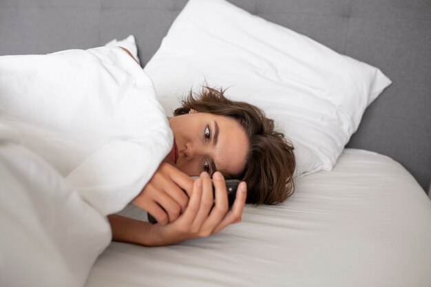 Mujer en la cama con teléfono inteligente