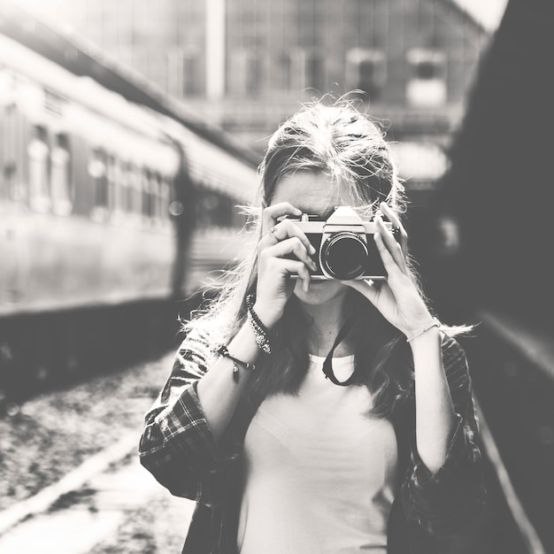 Mujer con cámara tomando fotos en escala de grises de la estación de tren