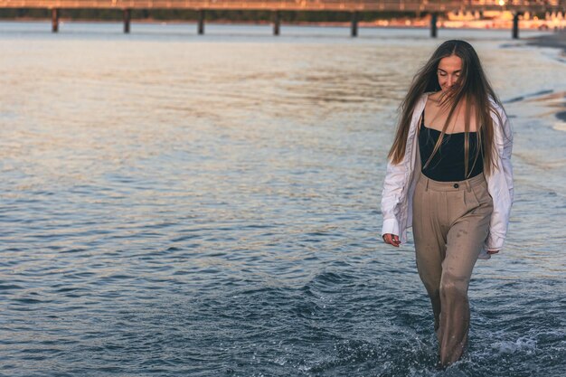 Una mujer camina descalza por el mar en el espacio de la copia al atardecer